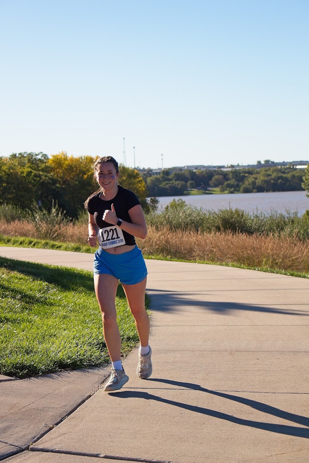 Runner in blue shorts giving a thumbs-up on a lakeside path.