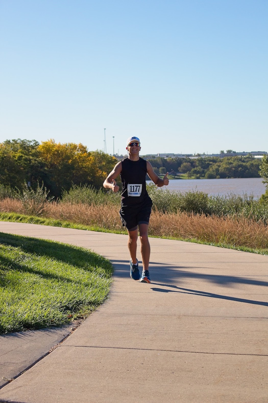 Runner wearing a cap and sunglasses on a lakeside path.